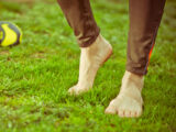 Mann hat seine Laufschuhe ausgezogen und geht barfuß auf einer grünen Wiese