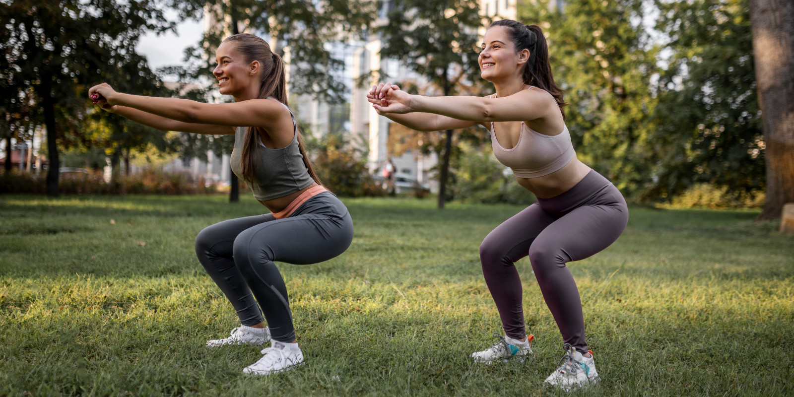 Zwei junge Frauen machen Kniebeugen beim Cathelistic Workout im Park