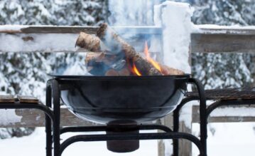 Grill mit Feuerholz in Schneelandschaft im Winter