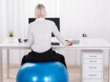 Frau sitzt am Schreibtisch auf einem Gymnastikball, um ihren Po zu trainieren