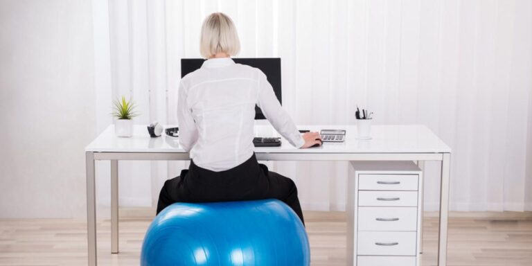 Frau sitzt am Schreibtisch auf einem Gymnastikball.