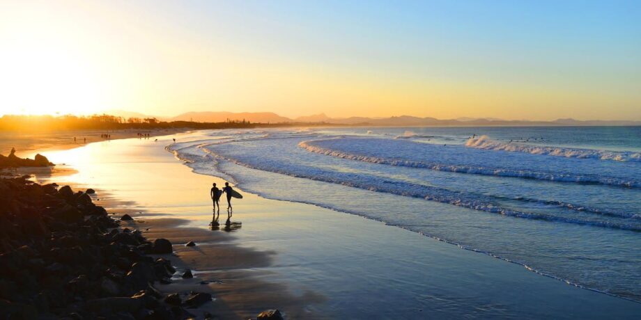 Surfer spazieren mit ihren Surfbrettern am Strand entlang und schauen in den Sonnenuntergang.