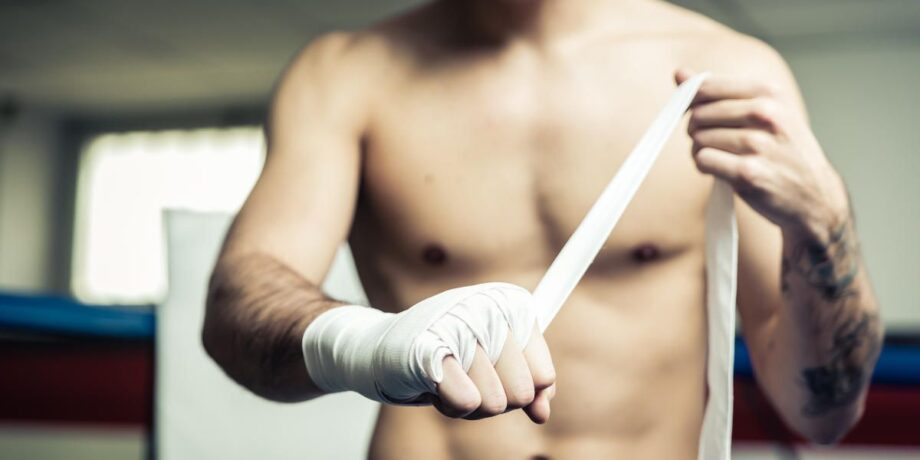 Mann bindet eine Boxbandage um seine Hand als Vorbereitung auf sein Kampfsporttraining