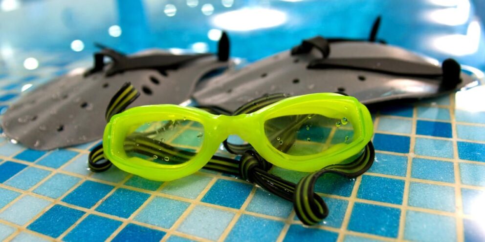 Taucherbrille und Schwimmflossen liegen am Beckenrand eines Schwimmbades