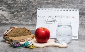 Holzbrett mit Brot, Apfel und einem Glas Wasser steht vor einem Kalender, in dem die Fastenzeit vermerkt ist