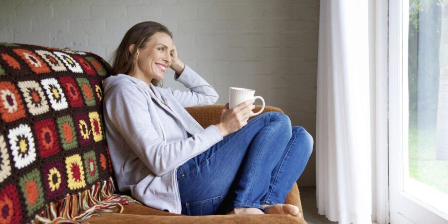 Frau sitzt auf der Couch mit eine Teetasse und blickt entspannt aus dem Fenster