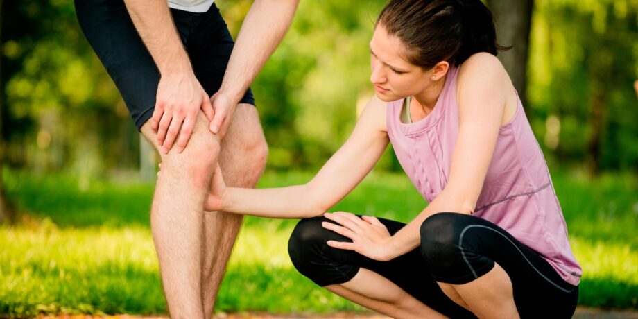 Läuferin schaut sich das Knie ihres Laufpartners genauer an, da er äußere Knieschmerzen hat.