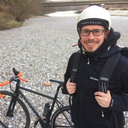 Felix steht neben seinem Fahrrad an einem Flussbett