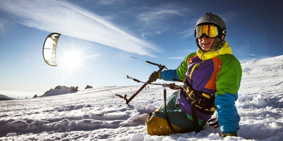 Sportlerin macht eine Pause beim Snowkiten und sitzt glücklich im Schnee.