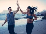 Frau und Mann laufen motiviert am Strand und geben sich ein High Five