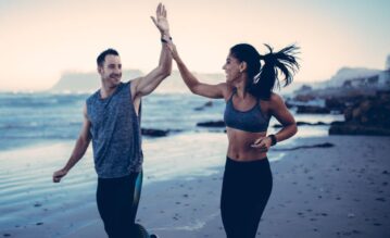 Frau und Mann laufen motiviert am Strand und geben sich ein High Five