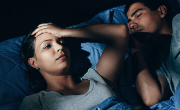 Frau liegt wach im Bett während ihr Mann neben ihr schläft