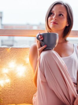 Frau sitzt mit einem Kaffee auf ihrem Balkon und trinkt einen Kaffee