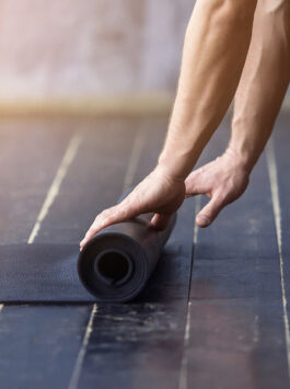 Mann rollt seine Yogamatte auf dem Boden aus