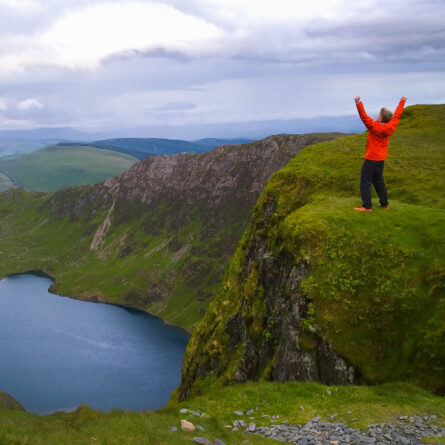 Mann steht auf einem Berg und blickt auf das Fjord hinunter