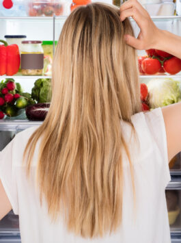 Frau steht vor dem Kühlschrank und überlegt, was sie essen soll