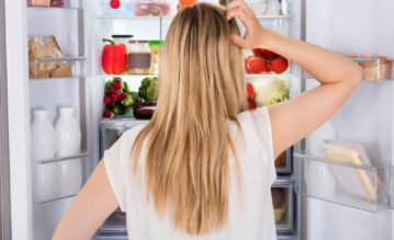 Frau steht vor dem Kühlschrank und überlegt, was sie essen soll