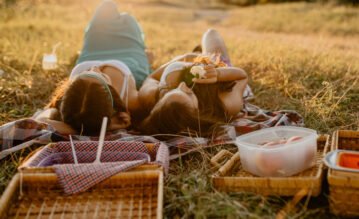 Zwei Frauen liegen im Sommer auf einer Picknickdecke auf einer Wiese