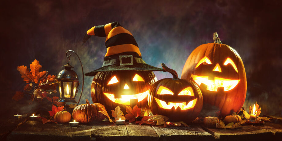 Leuchtende, gruselige Halloween Kürbisse mit Herbstdekoration stehen auf einem Tisch.