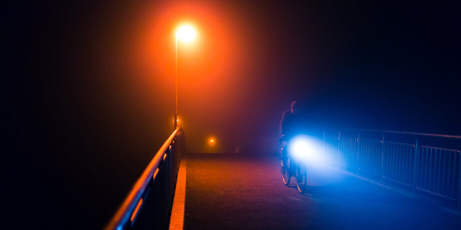 Radfahrer fährt nachts mit LED-Beleuchtung am Fahrrad über eine Brücke