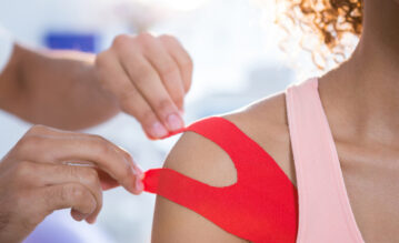 Bei einer Frau wird rotes Kinesio-Tape an der Schulter vom Arzt angebracht