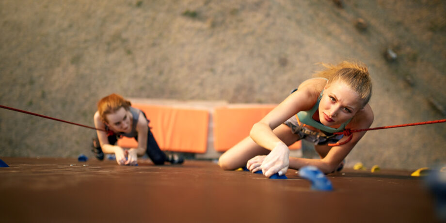 Sportlerinnen klettern mit Sicherung eine Boulderwand hoch.