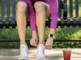 Frau mit einer vivoactive Smartwatch von Garmin sitzt auf einer Parkbank und bindet sich ihre Laufschuhe zu
