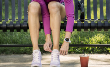 Frau mit einer vivoactive Smartwatch von Garmin sitzt auf einer Parkbank und bindet sich ihre Laufschuhe zu