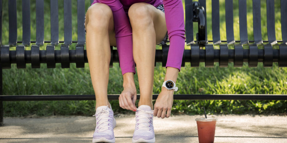 Frau mit einer vivoactive Smartwatch von Garmin sitzt auf einer Parkbank und bindet sich ihre Laufschuhe zu