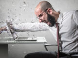 Wütender Mann schlägt mit einer Faust gegen seinen Laptop