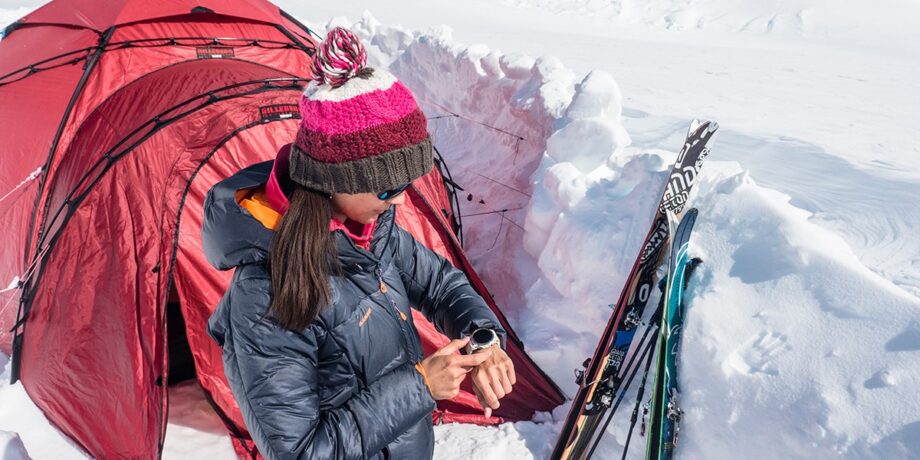 Vicky vor Ihrem Zelt im Schnee, mit Blick auf Ihre Garmin fēnix 5X Plus.