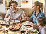 Familie mit zwei Kindern sitzen gemeinsam am Essenstisch und isst zu Mittag