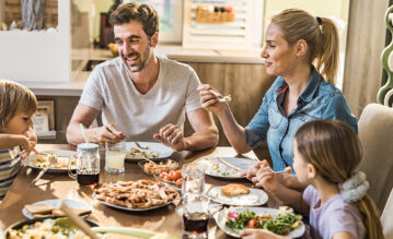 Familie mit zwei Kindern sitzen gemeinsam am Essenstisch und isst zu Mittag