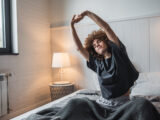 Junge Frau dehnt sich nach dem Aufwachen im Bett