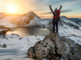 Frau hat beim Winterwandern einen Berg erklommen und schaut über die verschneite Landschaft