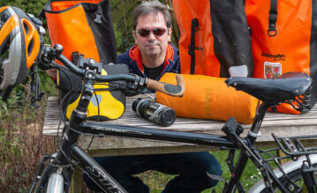 #BeatYesterday.org-Autor Christian Moeller sitzt mit seiner Ausrüstung für eine Radour an einem Holztisch