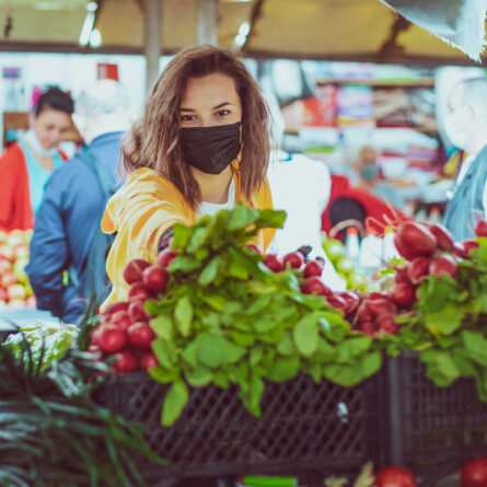 Junge Frau greift auf einem lokalen Markt an einem Stand zu Radieschen