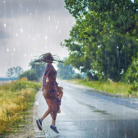 Junge Frau in einem Kleid tanzt auf der Straße im Regen
