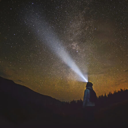 Mann leuchtet nachts mit seiner Kopflampe in den Sternenhimmel