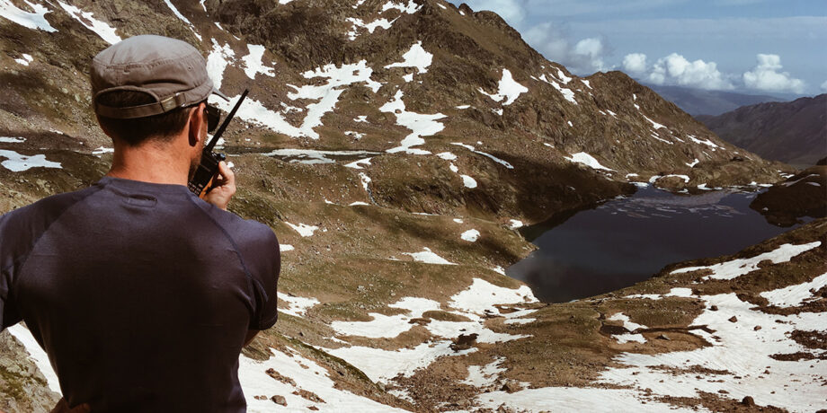 Guillaume steht vor den Bergen und spricht über ein Funkgerät mit der Bergwacht