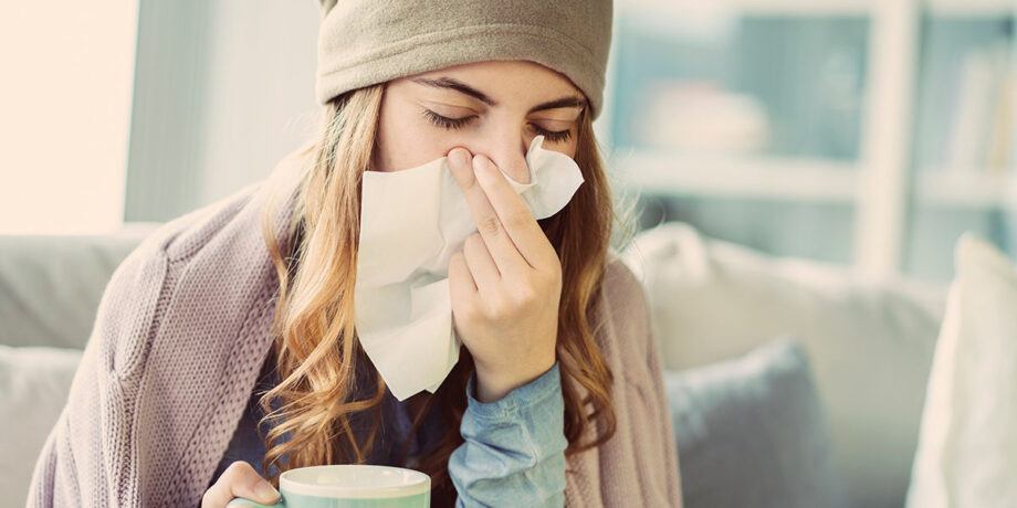Junge Frau mit Erkältung schnäubt sich die Nase