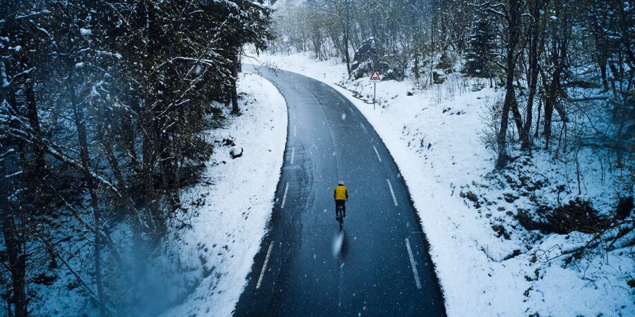 Lars Schneider fährt im Winter bei Schnee mit dem Fahrrad eine einsame Straße in Norwegen