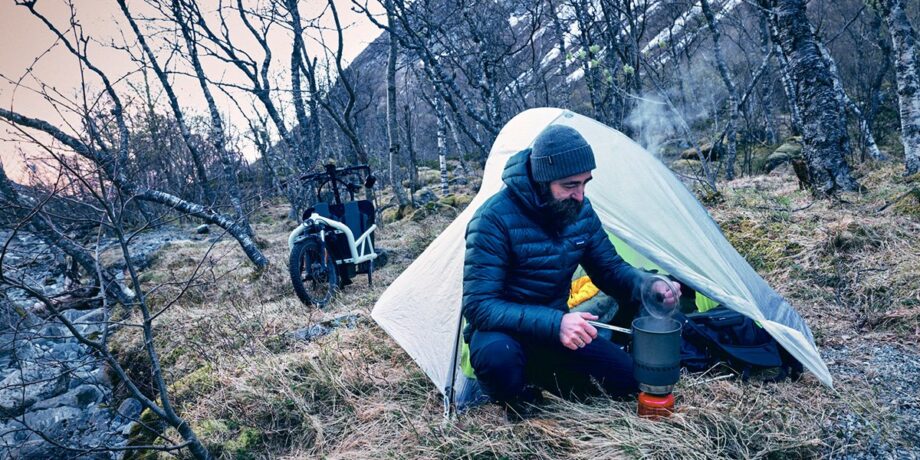 Lars Schneider sitzt neben seinem Zelt und kocht auf einem Campingkocher