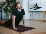 Mann macht zuhause Yoga-Übungen mit einem virtuellen Trainer