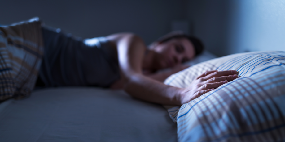 Frau liegt schlafend im Bett auf der Seite und streckt ihren Arm auf die andere Bettseite aus