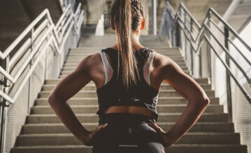 Frau steht in Sportbekleidung vor einer Treppe
