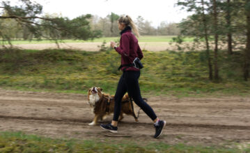 Junge Frau joggt mit ihrem Hund durch den Wald