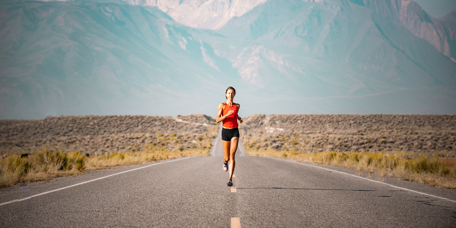 Ultr-Läuferin läuft auf einer Straße, hinter ihr eine Bergkulisse