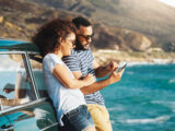Paar im Urlaub an einer Küste schaut auf Reiseapp
