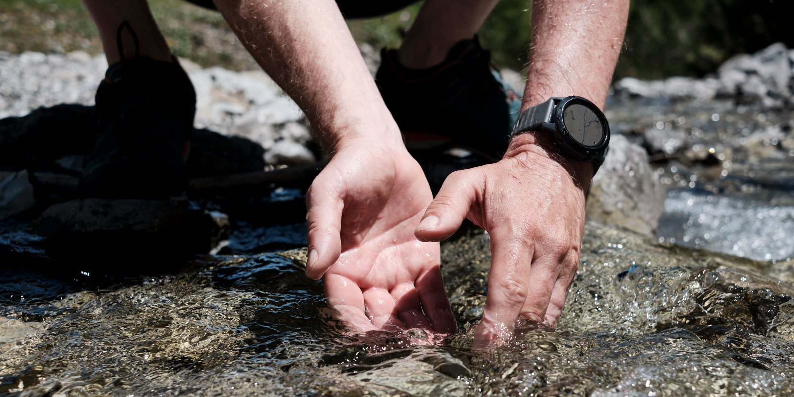 Mann wäscht seine Händer beim Wandern in einem klaren Fluss